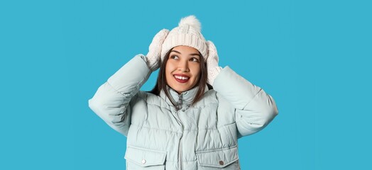 Young Asian woman in winter clothes on light blue background