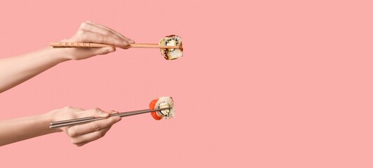 Hands holding chopsticks with different tasty sushi rolls on pink background with space for text