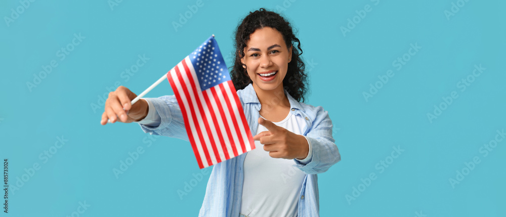 Wall mural Beautiful young happy African-American woman with USA flag pointing at viewer on blue background