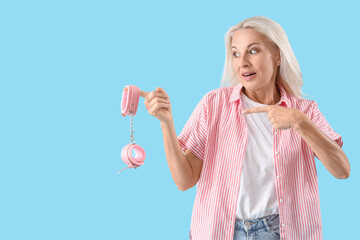 Mature woman pointing at handcuffs from sex shop on blue background