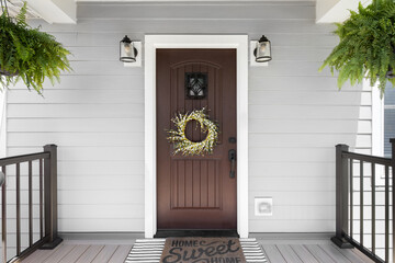 A wooden front door detail with grey vinyl siding, composite decking floor and raining, and lights mounted aside the doorway.