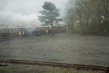 a vintage steam train and passenger carriages taking a bend in the track through rain and mist, ...