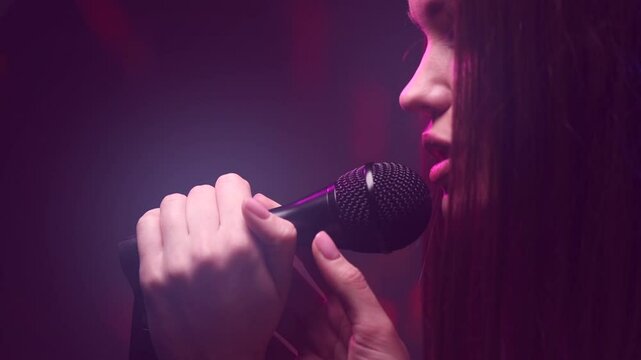 Singing Woman with Microphone. Karaoke bar. Beauty Glamour professional singer girl close-up. Stage. Rock star singer on music concert over colorful lights background. Song, pop music concept  
