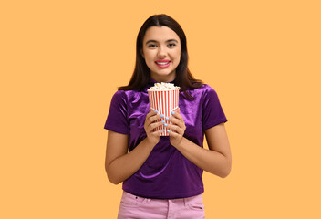 Beautiful young happy woman with bucket of popcorn on yellow background