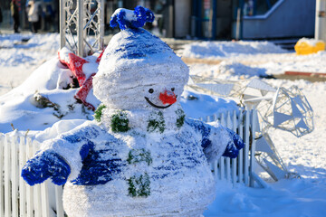 A snowman with a blue hat and scarf is standing in the snow, winter background or backdrop
