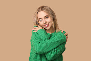 Young woman hugging herself on beige background