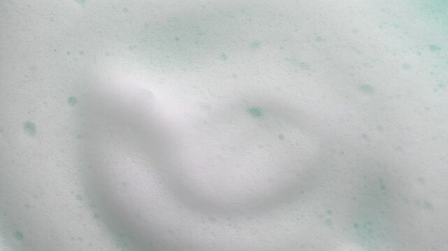 Foam texture backdrop on blue background. Liquid soap bubbles, Froth bubbles backdrop. Soap foam popping bubble rotating. Soap sud macro structure close-up. Clean, cleaning, washing, laundry