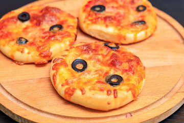 Three small pizzas with olives on top sit on a wooden cutting board