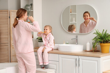Young mother and her little daughter brushing teeth near mirror in bathroom