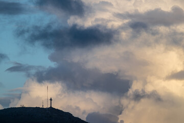 A cross is on top of a hill in the middle of a cloudy sky
