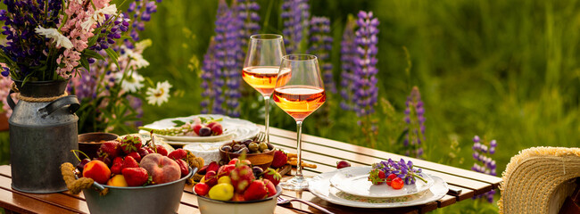 Banner. Beautiful elegant romantic dinner table decor, surprise day arrangement. Marriage proposal, engagement private party for two in a meadow. Sunset, golden hour. Cheese board, rose wine, fruits