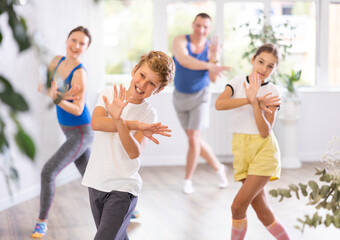 Obraz premium Excited preteen boy and girl exercising dance moves with their parents during dance class, family practicing dance with crossed hands in studio