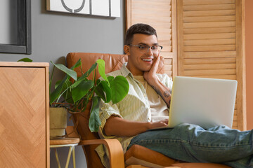 Male author with laptop in armchair at home