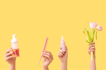 Female hands with different cosmetic products, beautiful tulips and hair comb on yellow background
