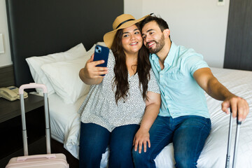 Couple relaxing on a bed in their hotel room after arriving from a vacation and taking a selfie