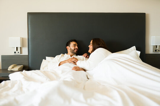 Joyful couple relaxes in bed in their hotel room, savoring precious moments together on their vacation - Powered by Adobe