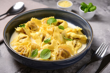 Bowl of boiled dumplings with sauce and basil on grey background
