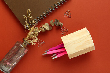 Vase of dried flowers, wooden holder with pens and notebook on red background