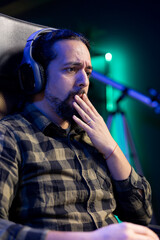 Shocked man sitting at a desk, watching a movie on portable computer while wearing headphones. Young guy listening to a podcast on wireless headset while surfing the net on laptop.