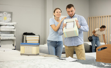 Couple study cross section structure of spring mattress in furniture store. They tests durability...