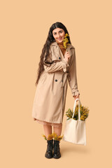 Beautiful young woman holding eco bag with mimosa flowers on beige background