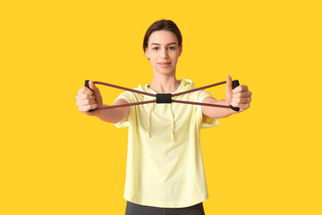 Beautiful young happy sporty woman with fitness expander on yellow background