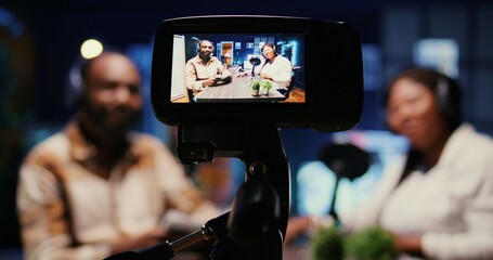 Focus on vlogging camera used by cohosts in blurry background streaming podcast during live debate on vlog channel. Close up of professional recording gear used by man and woman in studio to film show