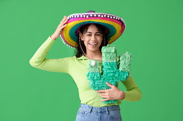 Happy young African-American woman in sombrero hat with pinata in shape of cactus on green...