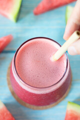 Watermelon smoothie glass with bamboo straw and sliced fruit on wooden table. Top view. Cold summer...
