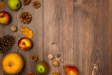Autumn harvest. Pumpkin, pears, apples, nuts, pine cones, and leaves on wooden background. Copy space, top view
