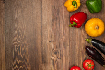 Pumpkins, eggplants, tomatoes and peppers of different colors on wooden background. Autumn harvest. Copy space, top view