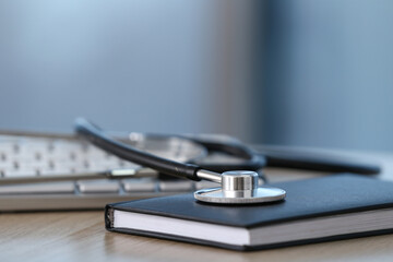 Stethoscope, notebook and keyboard on wooden table, closeup