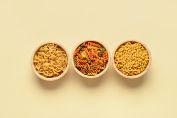 Bowls with different tasty uncooked pasta on beige background