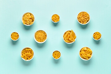 Bowls with different tasty uncooked pasta on blue background