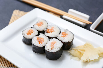 Plate with tasty sushi rolls and marinated ginger on black grunge background, closeup