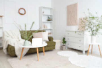 Stylish room with green sofa, coffee table and blooming branches, blurred view