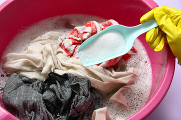 Woman in rubber gloves adding laundry detergent to clothes in plastic basin, closeup