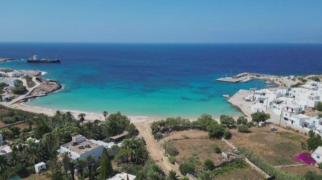 A picturesque aerial view of Donousa Island in the Cyclades, Greece, featuring a pristine beach, sparkling turquoise waters, and a charming village with whitewashed houses.