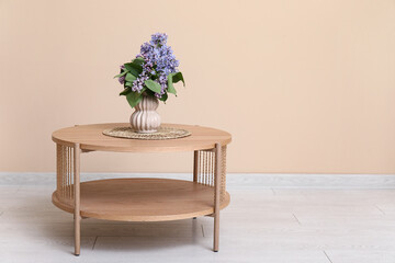 Vase with lilacs branches on coffee table near beige wall in room