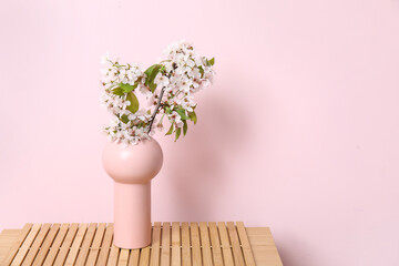 Vase with blossoming branches on shelf near pink wall in room