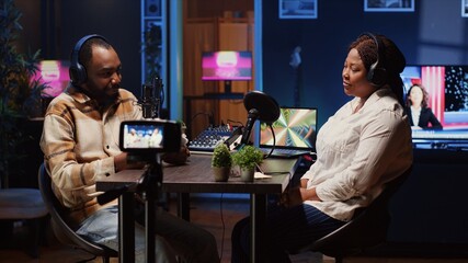 Radio show presenter using professional camera to record live conversation with man in personal studio. Influencer talking with woman, sharing interesting facts for fans at home