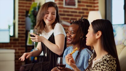 BIPOC women sitting on couch at home, gossiping about their boyfriends while enjoying glass of wine...