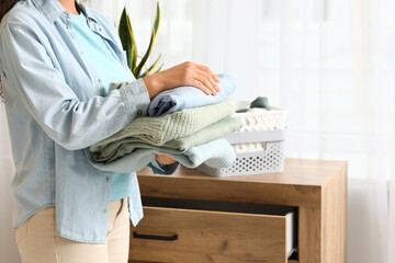 Beautiful young African-American woman with stack of clean clothes in bedroom, closeup