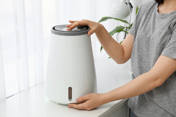 Young woman turning on modern humidifier on chest of drawers in room, closeup