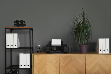 Modern printer and palm tree on commode near dark wall in office
