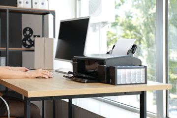 Fototapeta premium Businesswoman with computer and printer working at table in office, closeup