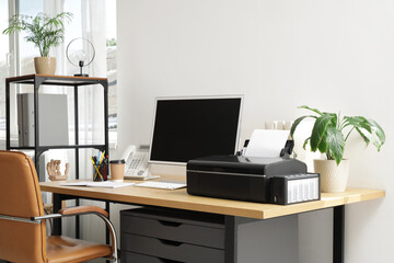 Modern workplace with computer and printer near light wall in office