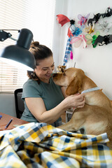 Dog kisses smiling woman who measures his neck for a scarf.