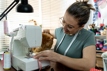 smailing woman working on her sewing machine in a sewing shop with cat