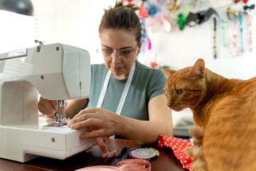 woman working on sewing machine while her cat watches